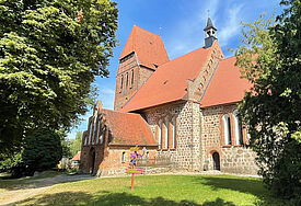 Wie ein Kulturfestival in einer Kirche ein Dorf zum Aufblühen bringt Eine alte Feldsteinkirche umgeben von großen Bäumen und Rasenflächen