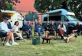 Gemeinde in Pommern bietet Campern einen Stellplatz: Promi-Team hat es ausprobiert Im Kreis auf Stühlen auf dem Rasen sitzt die Moderatorin Bettina Tietjen (Mitte), die mit ihrem Wohnmobil Station bei Pastorin Silke Kühn in Kartlow (3.v.li) machte. Mit dabei waren die Promi-Camper und -Camperinnen Axel Schulz, Isabel Varell, Leo Reisinger, Ariana Baborie und Pascal Hens, genannt „Pommes“. Im Hintergrund die Kartlower Johanniskirche.