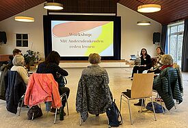 Was helfen kann, um mit Andersdenkenden ins Reden zu kommen Menschen sitzen bei einem Workshop im Stuhlkreis und schauen auf einen Monitor