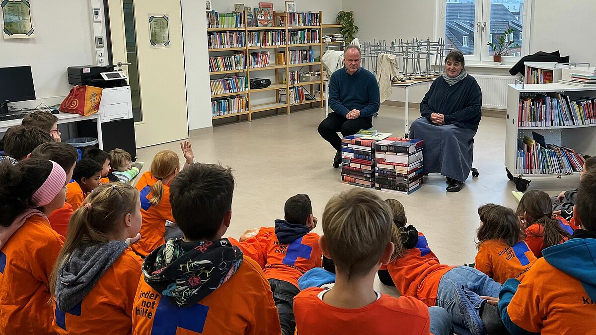 Bischof Tilman Jeremias liest den Kindern beim Vorlesemarathon vor. Die Veranstaltung ist Teil der Aktionswochen gegen Kinderarbeit. Neben ihm sitzt Gemeindepädagogin Kerstin Blümel, die junge Menschen seit 30 Jahren für das Thema Kinderarbeit sensibilisiert. 