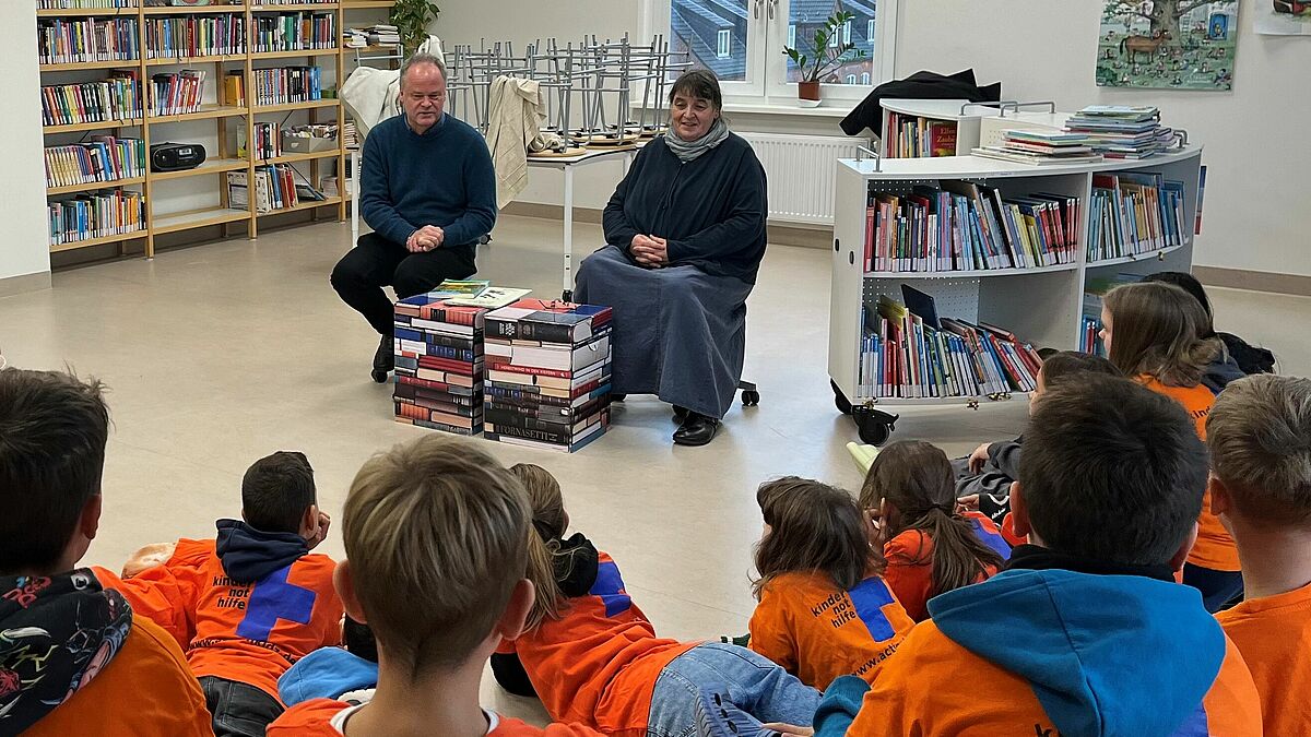 Bischof Tilman Jeremias liest den Kindern beim Vorlesemarathon vor. Die Veranstaltung ist Teil der Aktionswochen gegen Kinderarbeit. Neben ihm sitzt Gemeindepädagogin Kerstin Blümel, die junge Menschen seit 30 Jahren für das Thema Kinderarbeit sensibilisiert. 