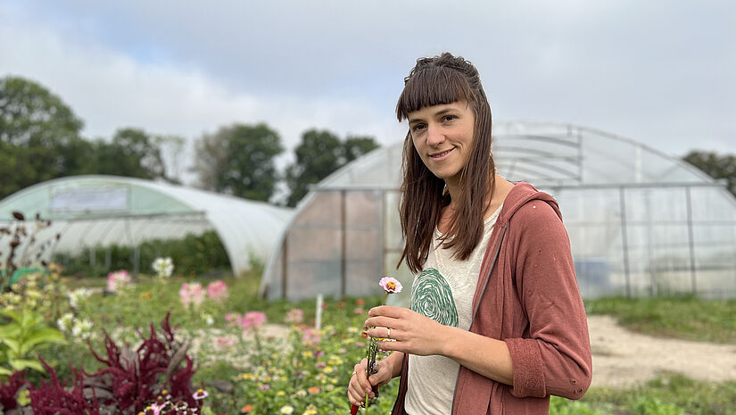 Eine Frau steht in einem Blumenfeld und hält eine Blume in der Hand.