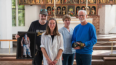 Hempels-Verkäufer Jan zeigt sein "Goldgräber-Bild" in der Nikolai-Kirche Kiel, in der es ausgestellt wird. Mit dabei sind Mitglieder des Hempels-Teams sowie der Fotograf Holger Förster. 