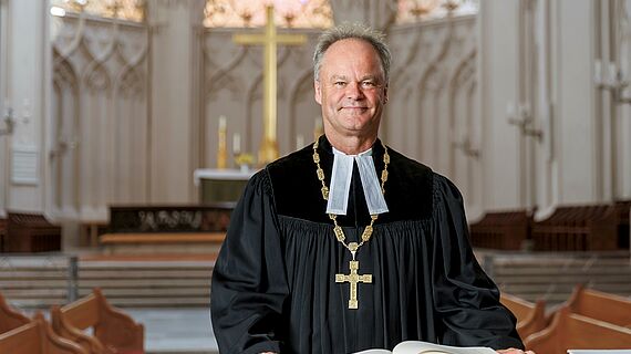 Bischof Jeremias trägt einen Talar und steht am Altar im Greifswalder Dom St. Nikolai