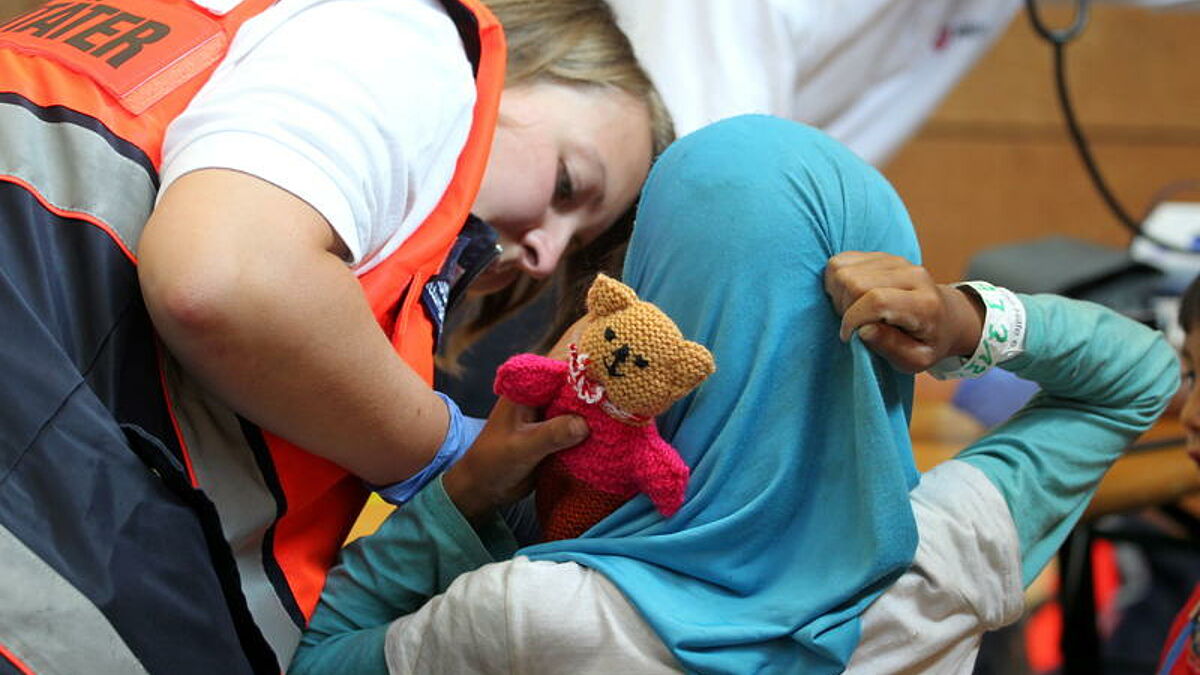 Erstaufnahmeeinrichtung (EAE) fuer Fluechtlinge in der Turnhalle der Reischleschen Wirtschaftsschule Augsburg am 02.08.15. Ein Fluechtlingskind wird medizinisch erstuntersucht. Als Willkommensgruss erhielt jedes Kind ein kleines Baerchen.