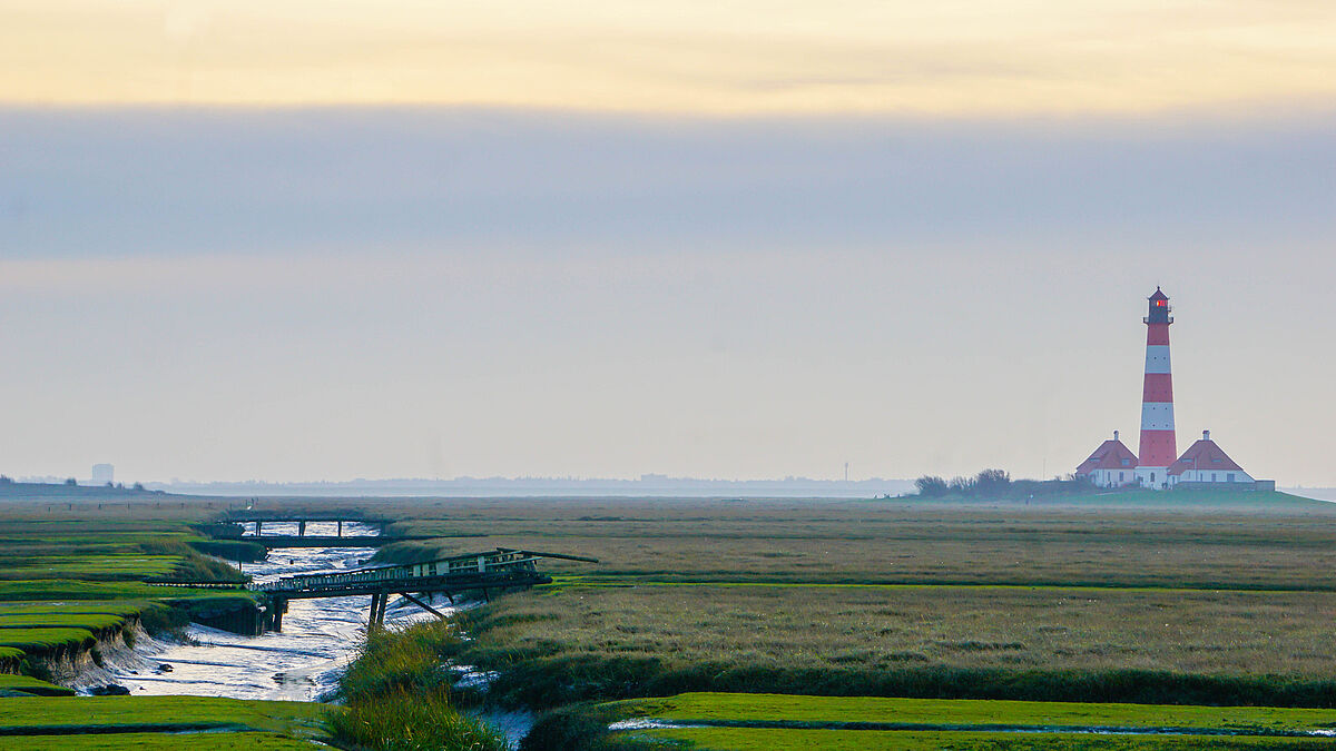 Der Leuchtturm Westerheversand in Nordfriesland liegt umgeben von der umliegenden Salzwiesenlandschaft an der Nordseeküste. 