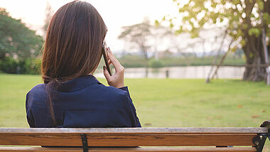 Eine Frau telefoniert mit dem Rücken zur Kamera auf einer Parkbank