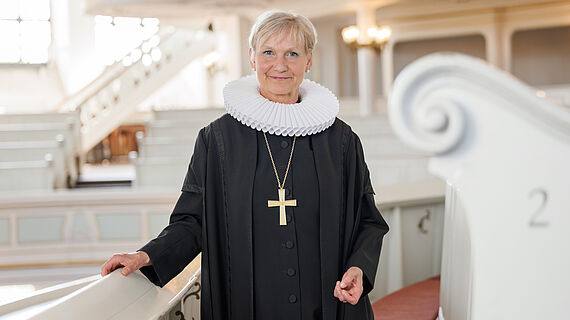 Bischöfin Fehrs führt neue Pastorin und neuen Pastor in ihren Dienst ein Bischöfin Kirsten Fehrs steht in Ornat und mit Bischofskreuz vor einer Sitzreihe in der Hamburger Hauptkirche St. Michaelis