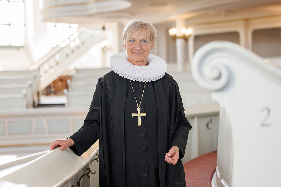 Bischöfin Kirsten Fehrs steht in Ornat und mit Bischofskreuz vor einer Sitzreihe in der Hamburger Hauptkirche St. Michaelis