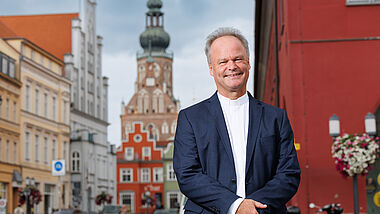 Bischof Jeremias steht im Anzug in Greifswald. Im Hintergrund. ist der Domturm zu erkennen.