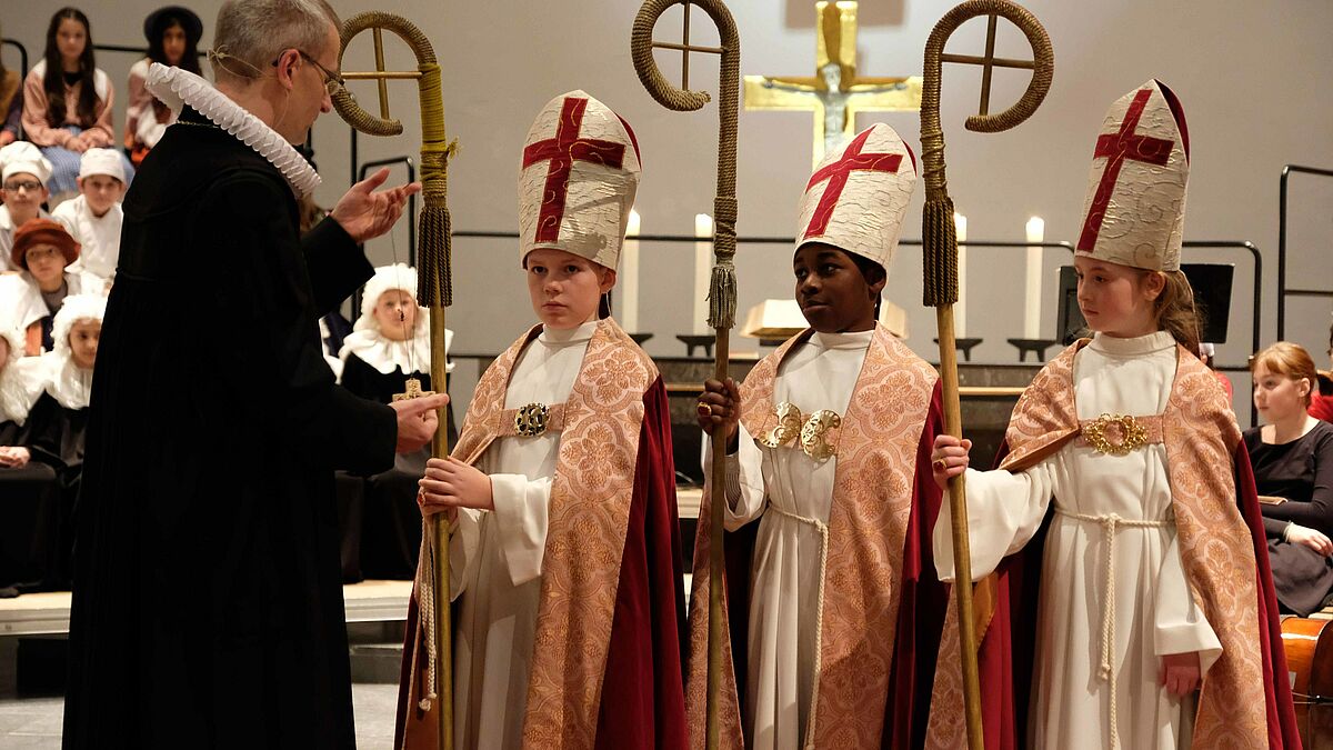 Hauptpastor Martin Vetter legt Christian Kratzsch (11), Raphael Owuso Opuko (10) und Mila Jandt (10) das Bischofskreuz um (von links)