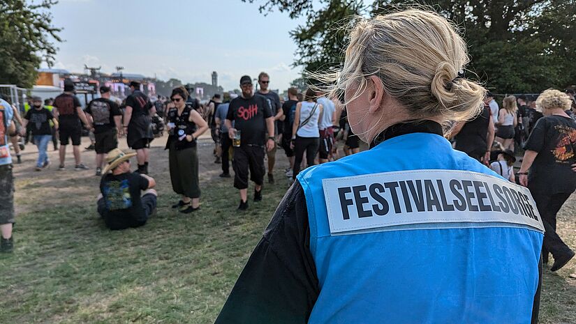 Festivalseelsorgerin in blauer Weste beobachtet erste Fans beim Aufbau ihrer Zelte.