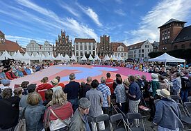 Auf dem Marktplatz breiten Bürger:innen und Kirchentagsteilnehmer:innen ein riesiges Friedenszeichen aus. 