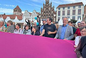 Auf dem Marktplatz breiten Bürger:innen und Kirchentagsteilnehmer:innen ein riesiges Friedenszeichen aus. 