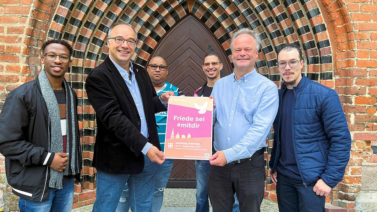 Bischof Jeremias (2.von rechts) lädt gemeinsam mit dem pommerschen Ökumenebeauftragten Gerrit Marx (2. von lenks) zum Friedenszeichen beim Kirchentag in Greifswald ein. Mit im Bild: Die vierköpfige südafrikanische Acapella-Gospelband UNISON. Sie wird unter anderem auf der Bühne auf dem Marktplatz auftreten.