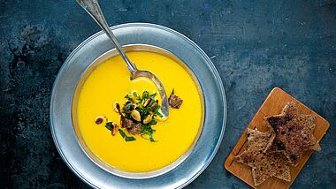 Im Bild zu sehen ist ein Teller Kürbis-Suppe neben zwei Stückchen geröstetem Brot, die als Sterne ausgestochen sind.