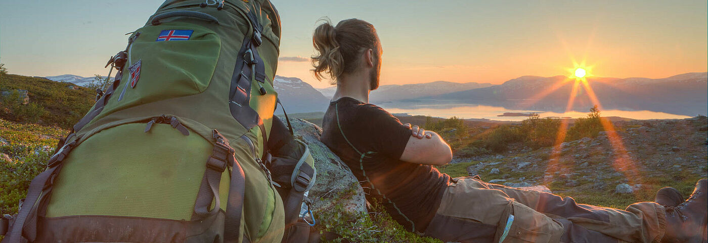 Ein Wanderer genießt die Ruhe auf einem Berg vor der Kulisse der untergehenden Sonne.