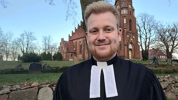 Malte Parlow steht in seinem schwarzen Talar vor der Kirche in Neustadt-Glewe