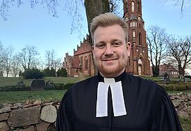 Malte Parlow steht in seinem schwarzen Talar vor der Kirche in Neustadt-Glewe