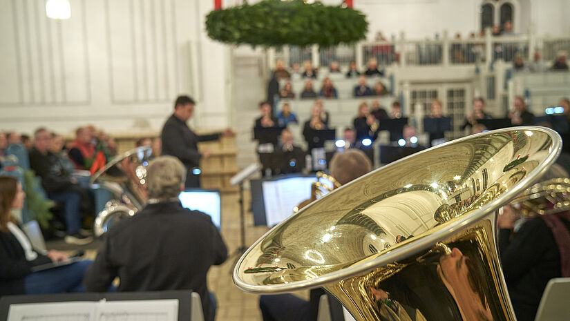 Musiker sitzen mit ihren Blasinstrumenten unter einem Adventskranz in einer Kirche.