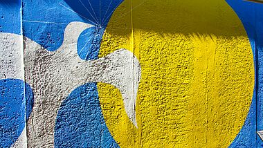 Graffitti zeigt eine Taube, die gen Sonne fliegt in den Farben der Ukraine 