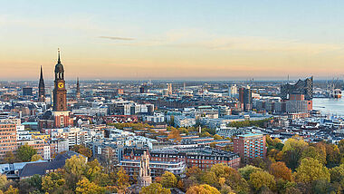 Blick auf Hamburg mit Michel, Hafen und Elbphilharmonie bei Sonnenuntergang.