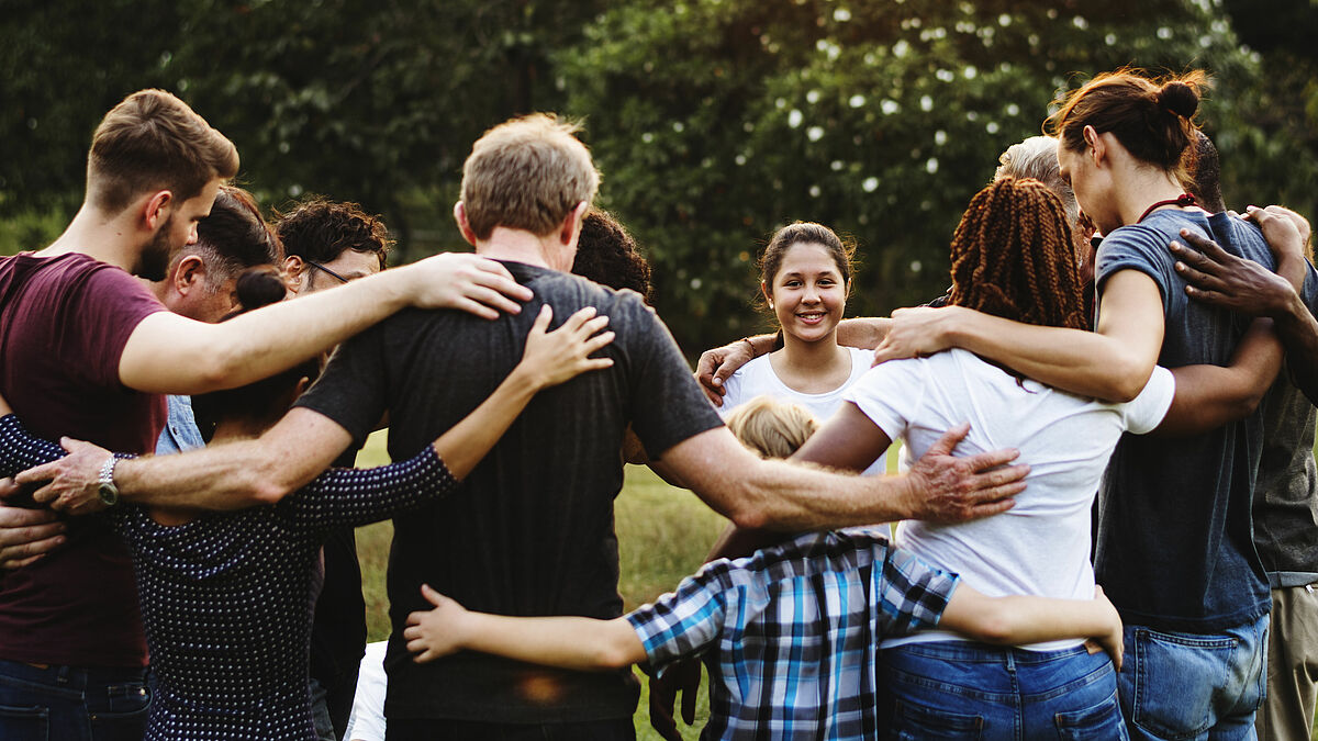 Eine Gruppe von Menschen draußen bilden einen Kreis, halten einander fest