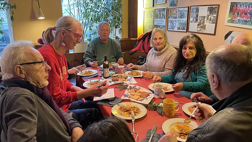 Menschen sitzen in einer Kneipe rund um einen Tisch und haben gefüllte Teller vor sich