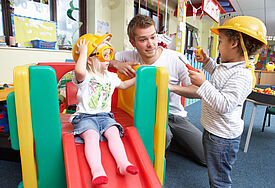 Ein junger Mann spielt mit zwei Kindern in einer Tageseinrichtung für Kinder.