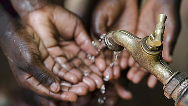 Hände, die sich um einen Wasserhahn drängen