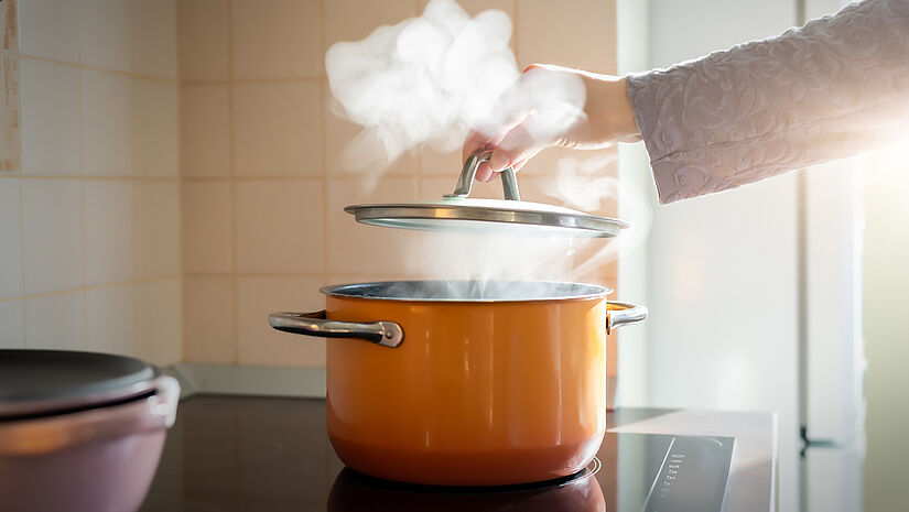 Ein orangefarbener Kochtopf steht dampfend auf einem Herd.