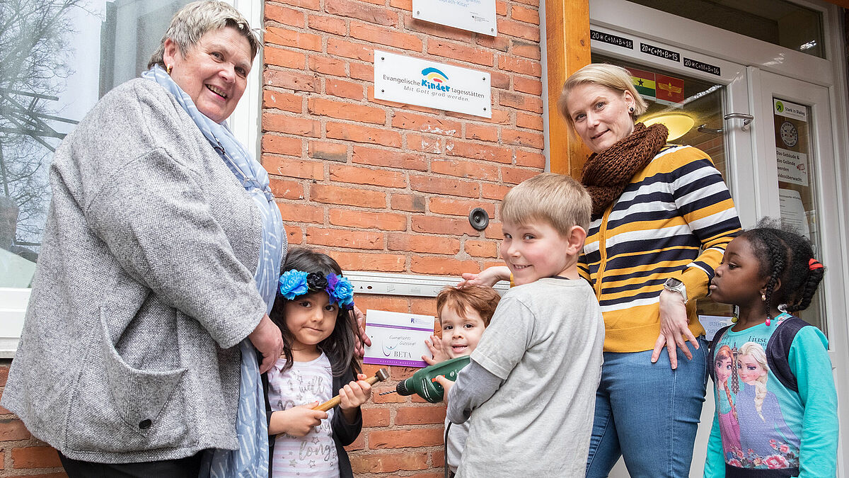 Schon mal gucken, wo das Gütesiegel seinen Platz am Eingang findet: Kinder der Ev. Kita Noahs Arche zusammen mit Leiterin Birgit Griesbach (links) und der Qualitätsbeauftragten Meike Roetz (rechts).