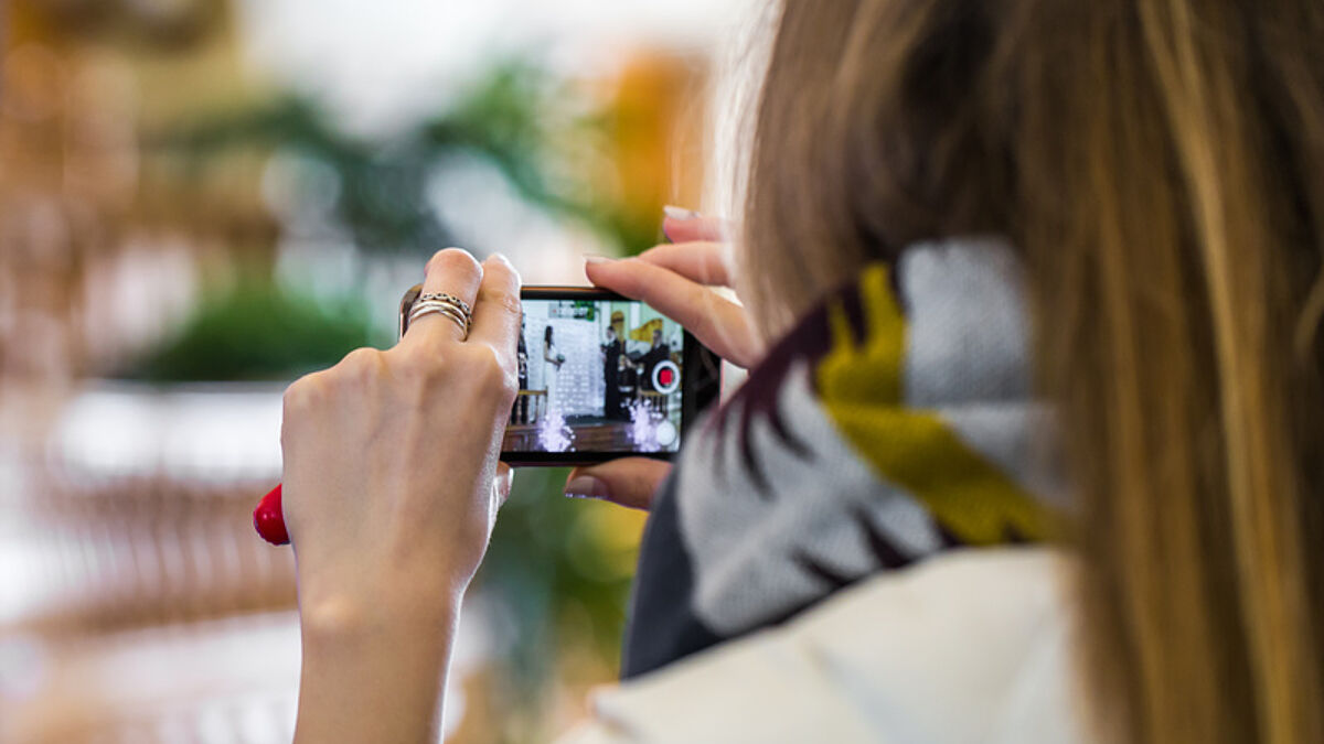 Junge Frau filmt mit ihrem Smartphone.